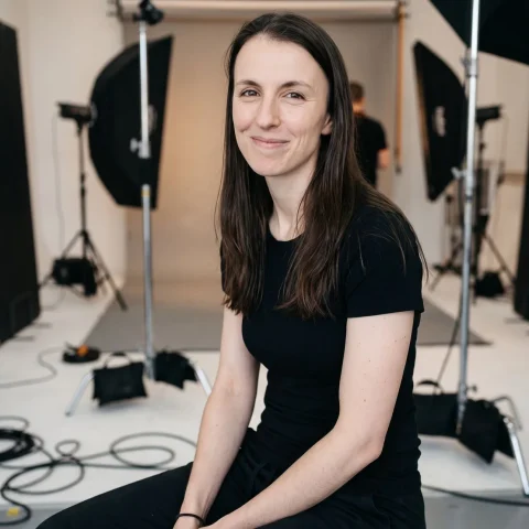 Seated professional studio portrait of an Allied Health Warrior mentor in black, with photography equipment in the background.